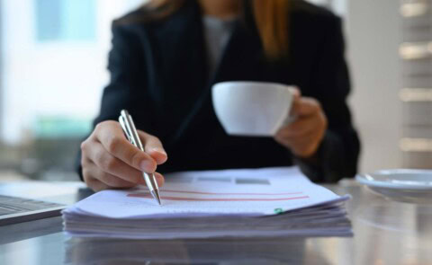Business woman's hands holding white coffee cup and reviewing papers
