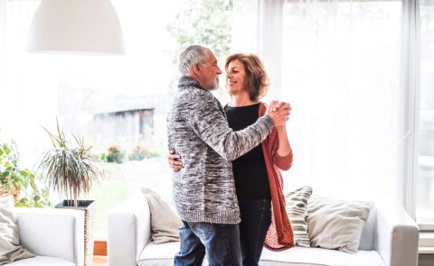 Couple dancing close in living room in front of window