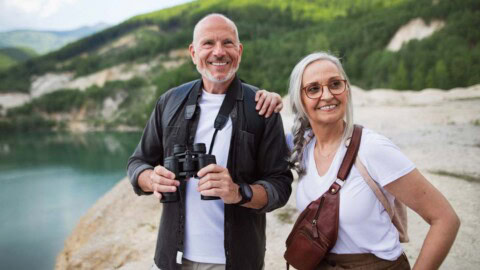Older couple standing outside by water with binoculars