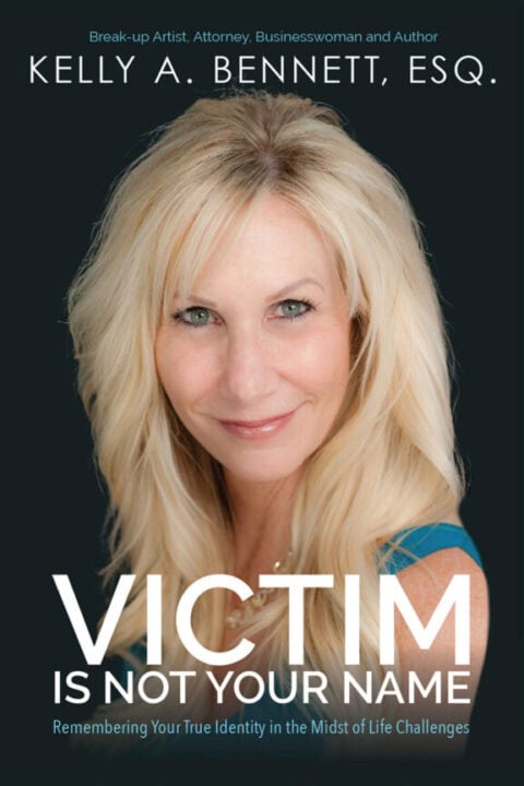 The cover of the book "Victim Is Not Your Name" by Kelly A. Bennett, Esq., featuring a close-up of the author with blonde hair and a confident expression, wearing a blue top. The subtitle reads, "Remembering Your True Identity in the Midst of Life Challenges."