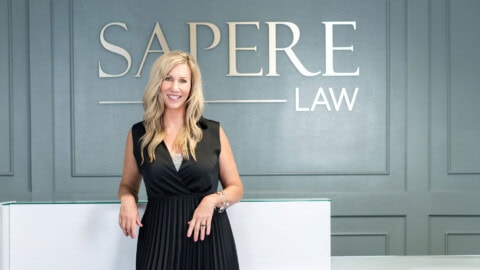 Woman in black dress standing in lobby in front of sign that says Sapere