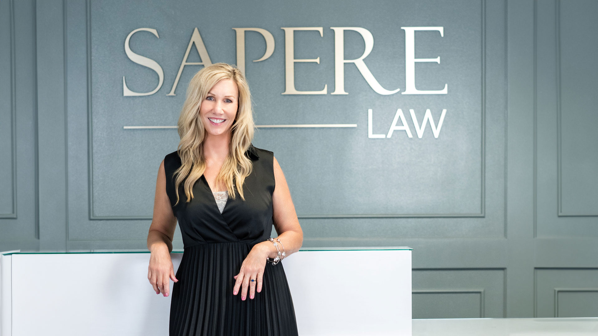 Woman in black dress standing in lobby in front of sign that says Sapere