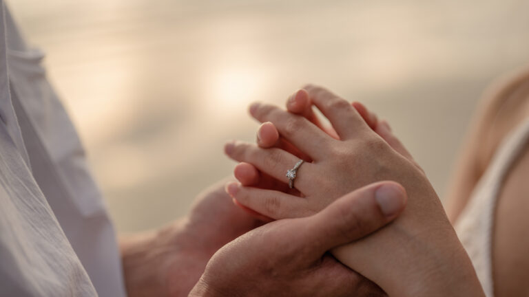 Close up man and woman holding hands with ocean in background