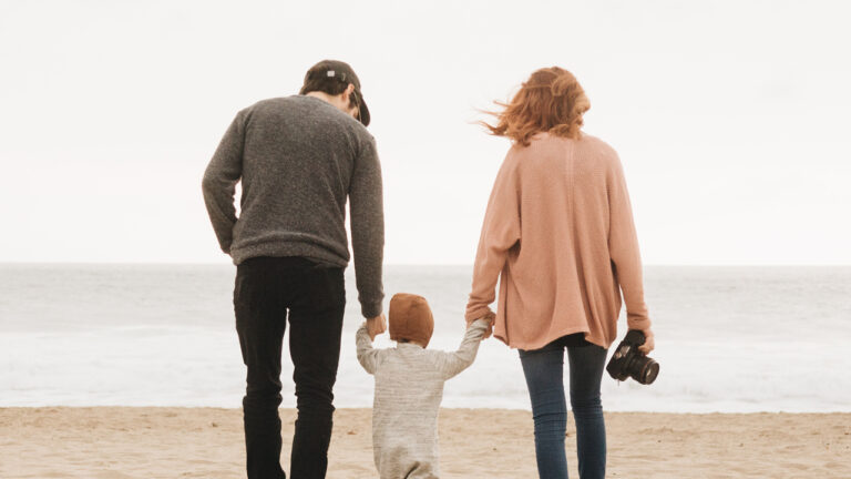 Two adults and a toddler walking on the beach